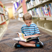Jongen op de grond in kleermakerszit met een boek op school in de bibliotheek